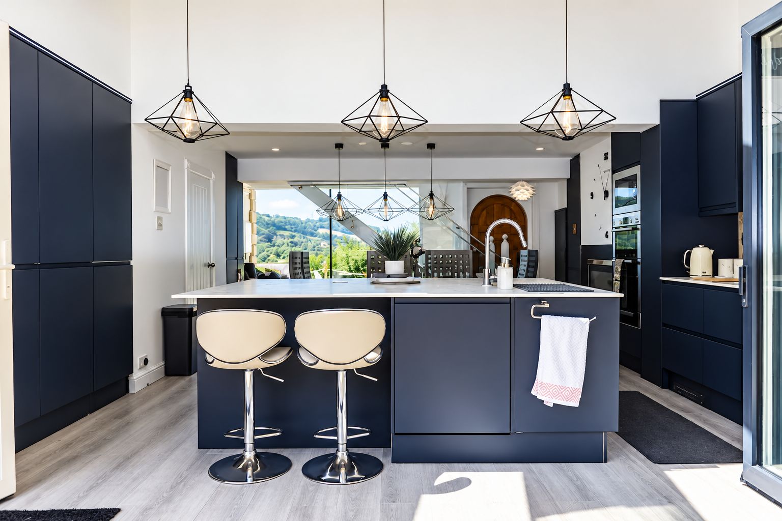 Una cocina moderna con una isla central, taburetes de bar, iluminación colgante y vistas al exterior.