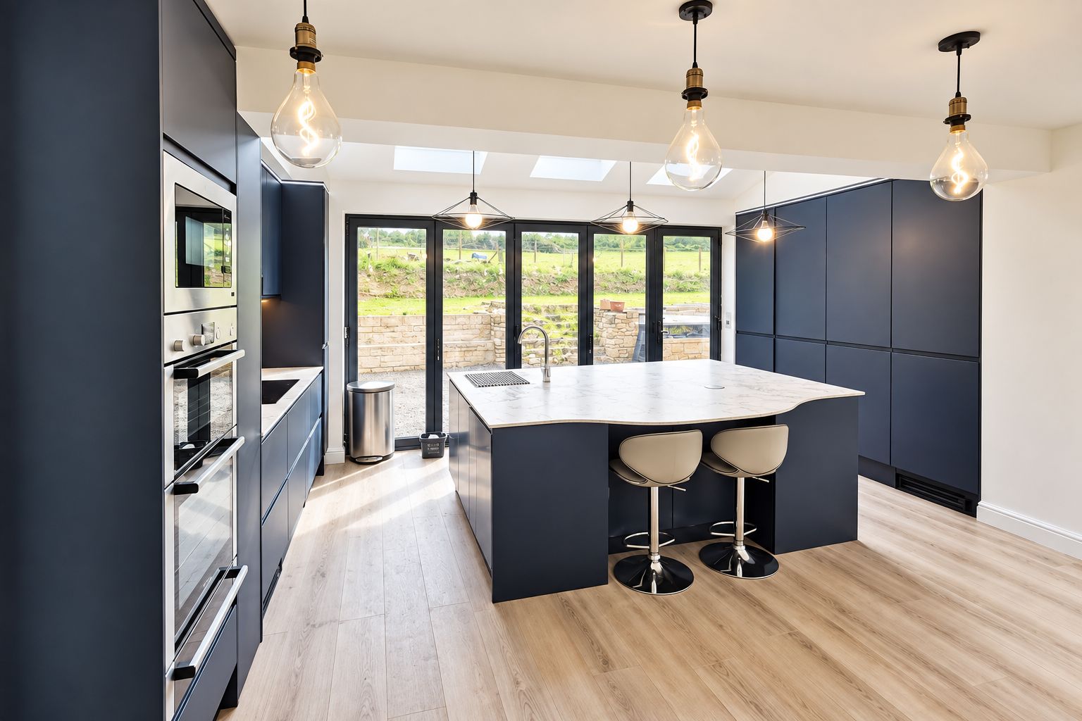Una cucina moderna con isola centrale, illuminazione a sospensione e vista panoramica attraverso ampie finestre.