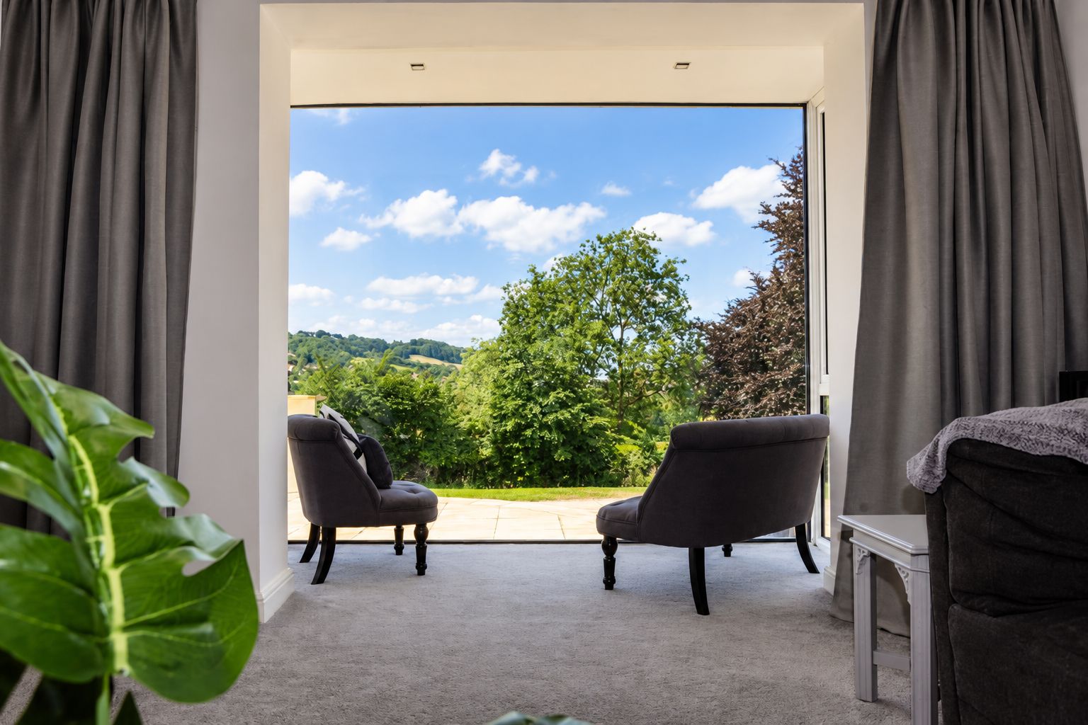 Habitación con vistas a un paisaje verde a través de un ventanal, dos sillas y una mesita.