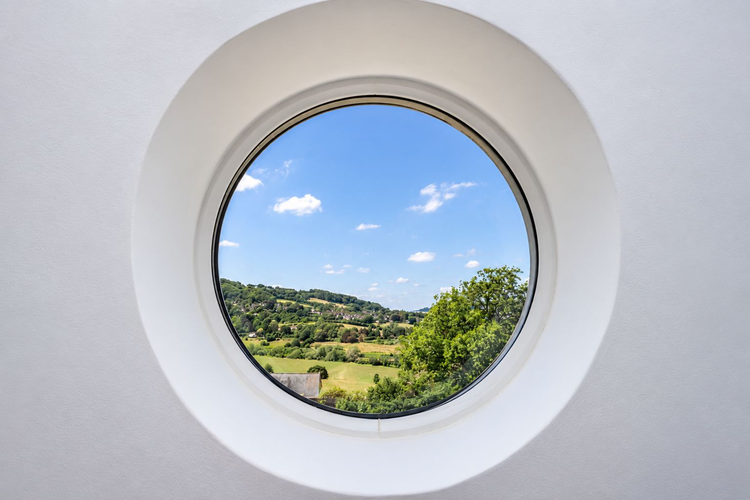 Een rond raam met een helder uitzicht op een groen landschap en heuvels.