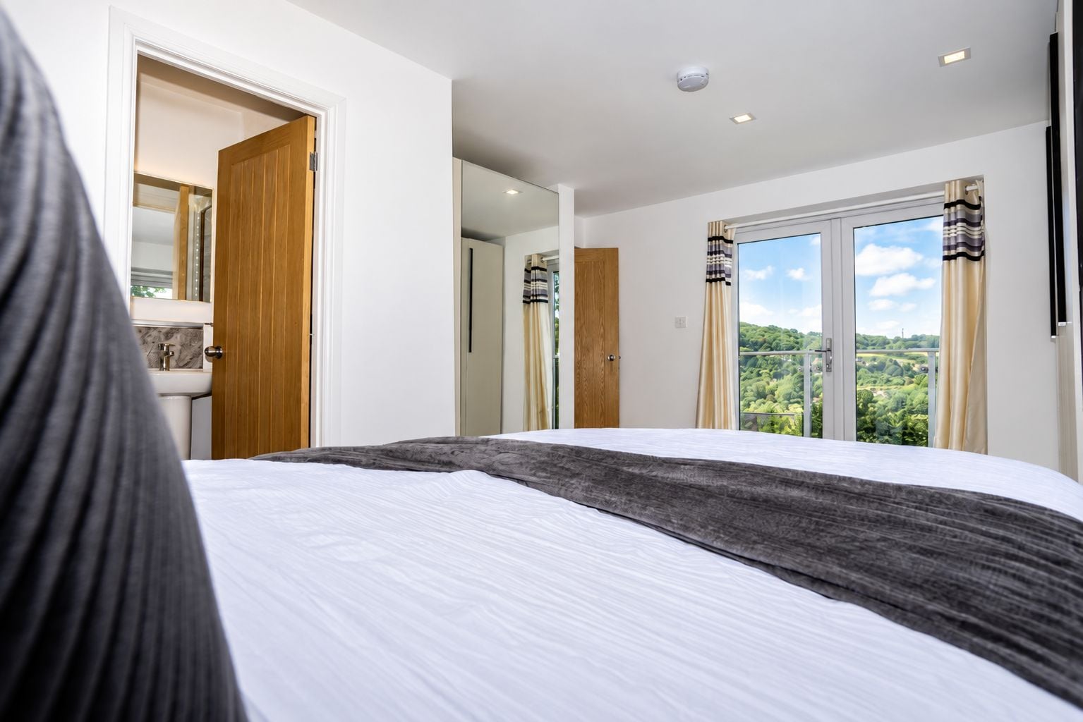 Un dormitorio con una cama grande, un baño con lavamanos y vistas a un paisaje verde por la ventana.