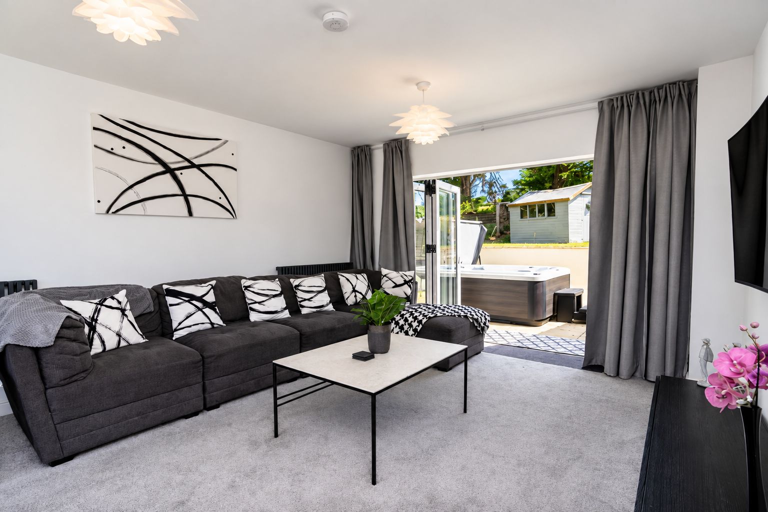 Ein modernes Wohnzimmer mit einem grauen Sofa, einem Couchtisch und einem großen Fenster mit Vorhängen.