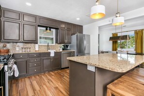 Eine moderne Küche mit dunklen Schränken, einem Edelstahl-Kühlschrank, Granit-Arbeitsplatten und Pendelleuchten.