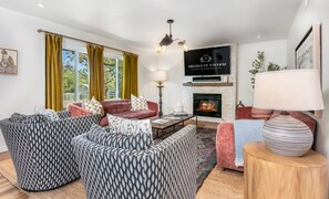 En rummelig stue med pejs, tv ophængt på væggen og et hyggeligt siddeområde med stribede sofaer.