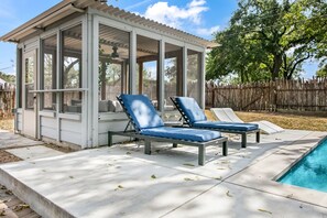 Ein überdachter Außenbereich mit zwei Liegestühlen und einem Pool.
