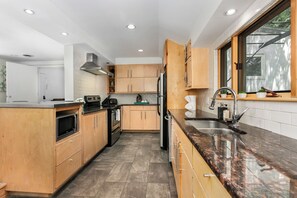 Een moderne keuken met houten kastjes, een granieten aanrechtblad, roestvrijstalen apparatuur en een raam dat voor natuurlijk licht zorgt.