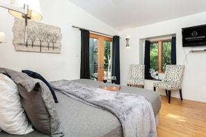 A modern bedroom with a bed, a desk, two chairs, a painting, and a television. - King-bed Fredericksburg hideaway with Wi-Fi, fire pit, and pet-friendly charm. (Fredericksburg)