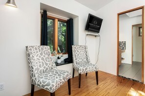 Ein Zimmer mit zwei gemusterten Stühlen, einem an der Wand befestigten Fernseher und einem Fenster mit Vorhängen.