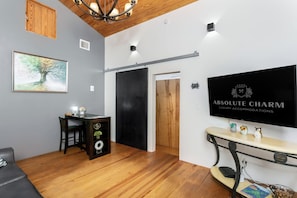 A modern hotel lobby with a wooden ceiling, a mounted television displaying 'ABSOLUTE CHARM LUXURY ACCOMMODATIONS', a desk with a plant, and a sofa. - King-bed Fredericksburg hideaway with Wi-Fi, fire pit, and pet-friendly charm. (Fredericksburg)