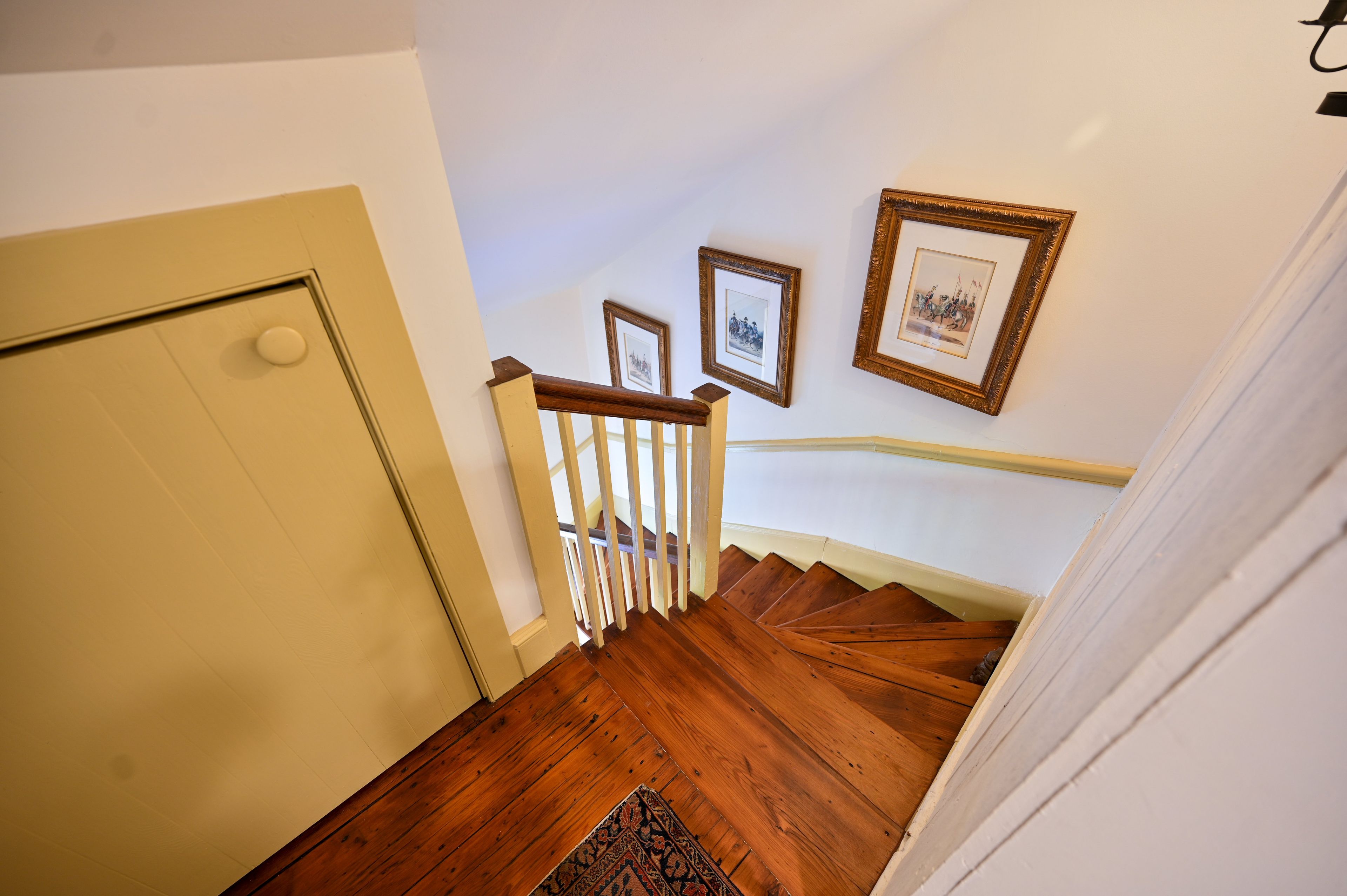 Un escalier en bois, avec une porte blanche en haut et un palier recouvert de moquette.