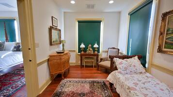 A bedroom with a bed, a dresser, a chair, a table with lamps, and a green door.