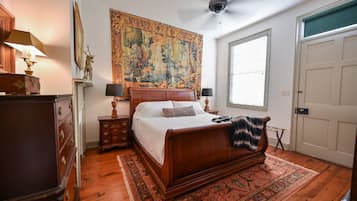A bedroom with a large bed, a ceiling fan, a tapestry, and a wooden dresser.