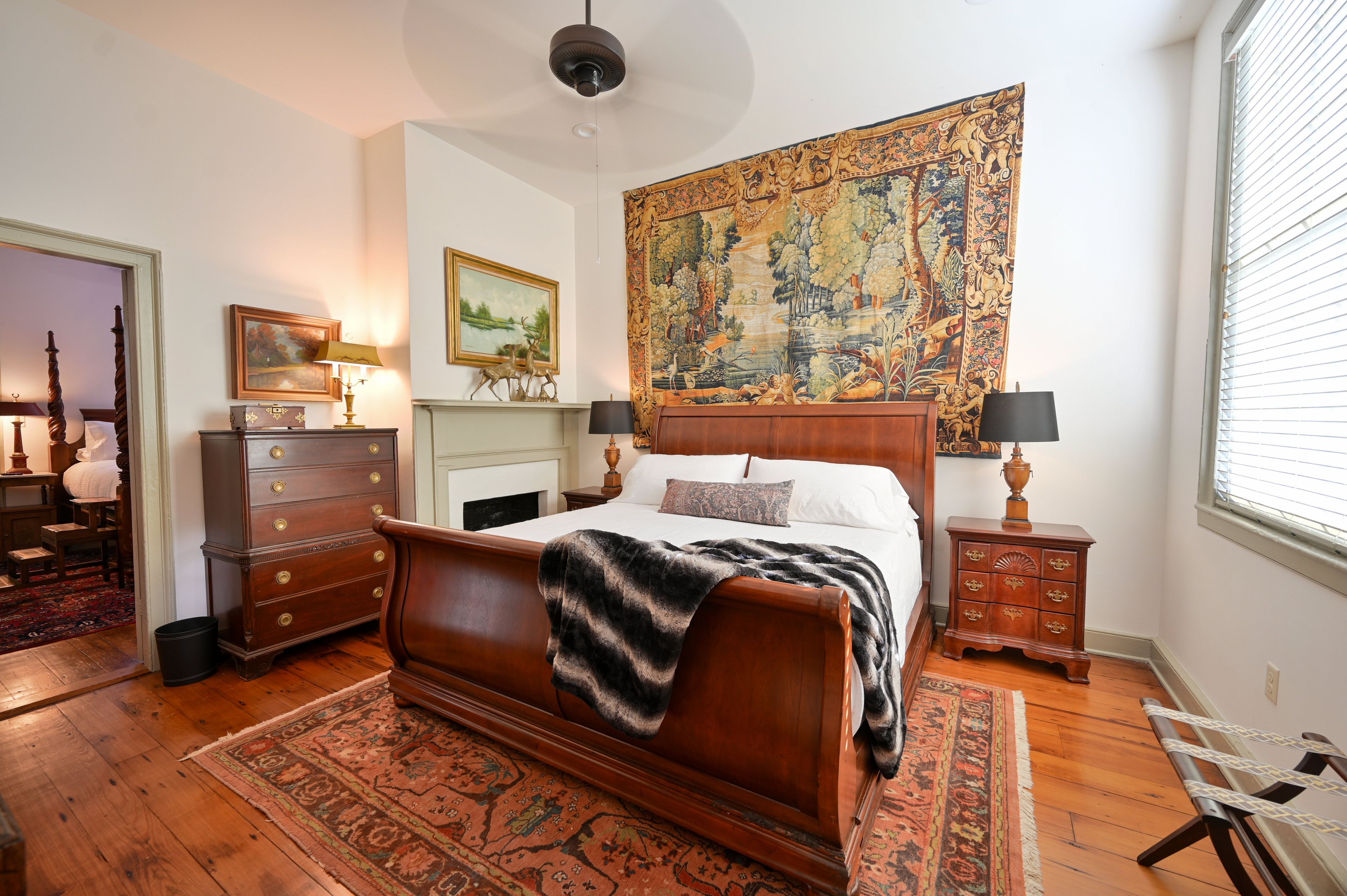 Un dormitorio con una cama grande, un aparador, una mesita de noche, un tapiz y una ventana con persianas.