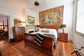Un dormitorio con una cama grande, un aparador, una mesita de noche, un tapiz y una ventana con persianas.