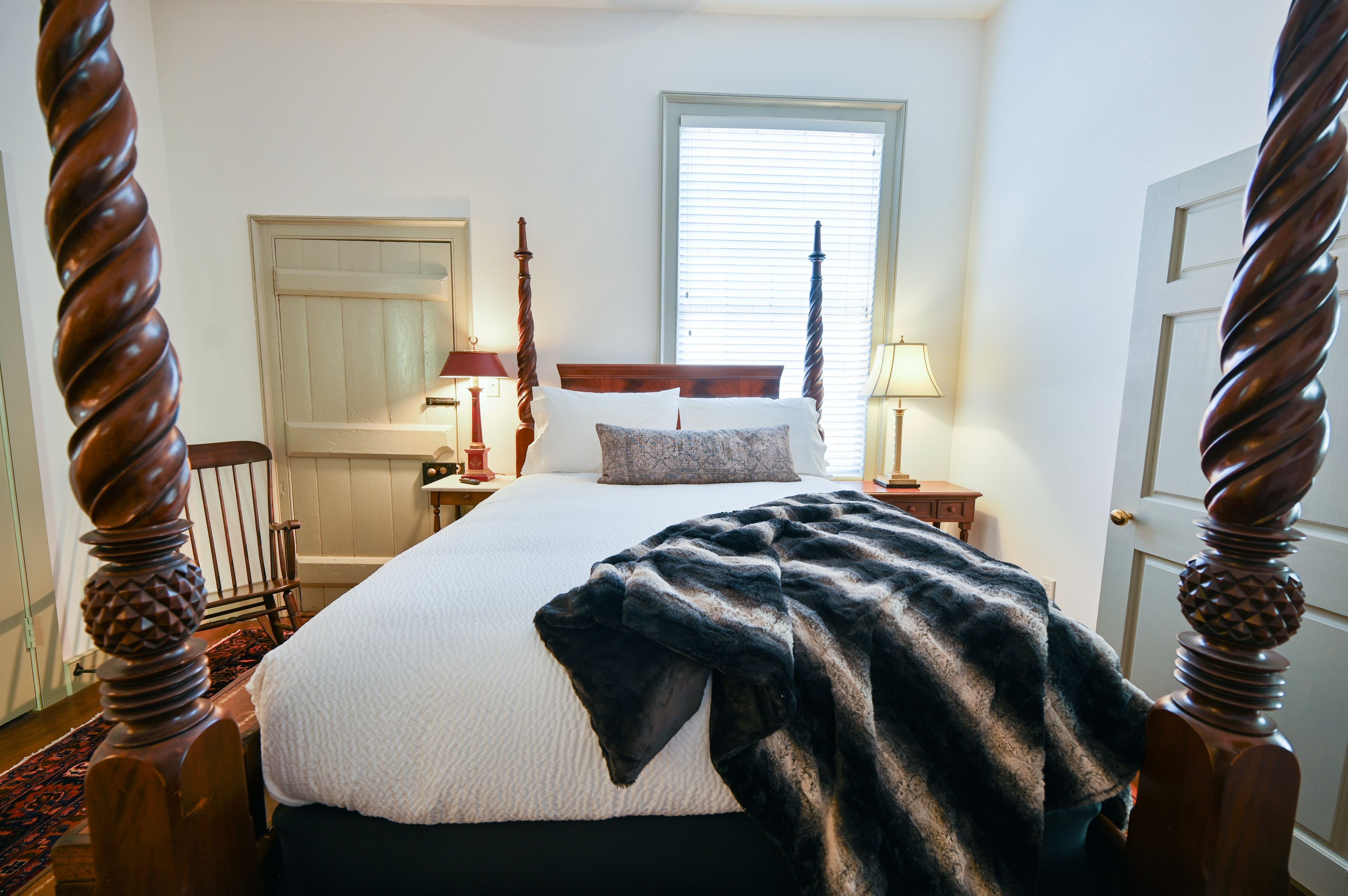 Une chambre à coucher avec un lit à baldaquin, une fenêtre avec des stores, une table de chevet avec une lampe et une porte.