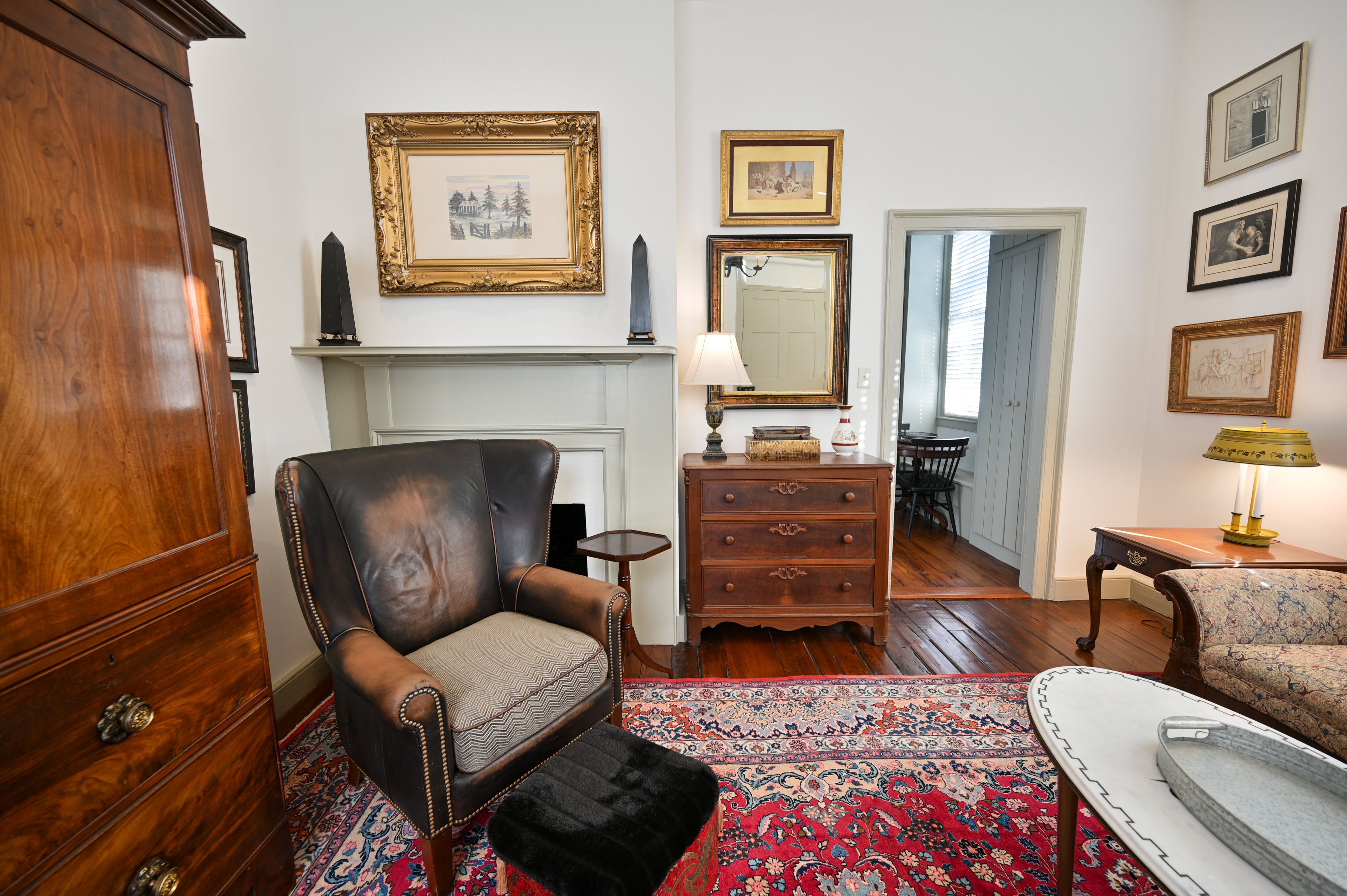 Un salón tradicional con un sillón de cuero, un aparador de madera, una chimenea y una colección de cuadros en la pared.