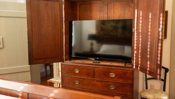 A wooden cabinet with a flat-screen TV on top, a small chair, and a bedside table.
