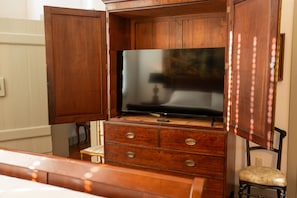 A wooden cabinet with a flat-screen TV on top, a small chair, and a bedside table.