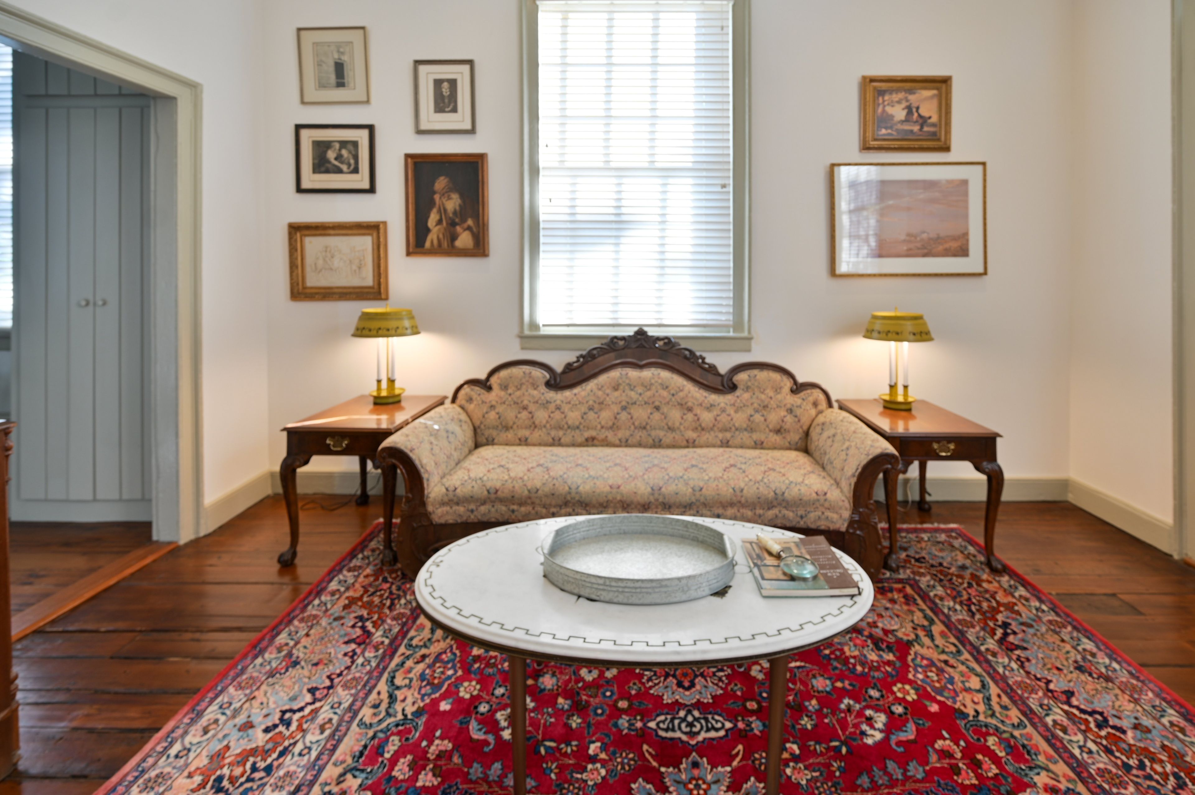 A room with a sofa, two lamps, a patterned rug, and framed pictures on the wall.