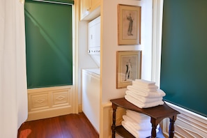 Ein Flur mit grüner Wand, Holzboden, einer weißen Tür und einem Stapel weißer Handtücher auf einem Holztisch.