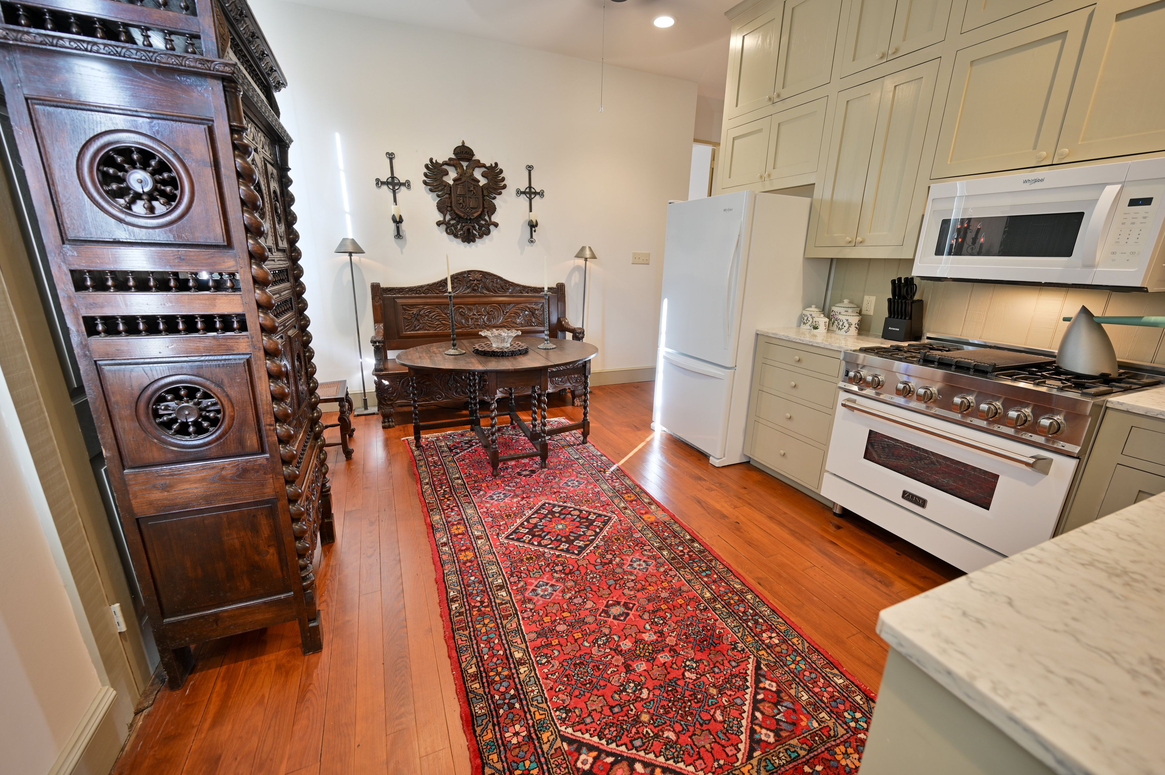 A kitchen with wooden cabinetry, a stove, a refrigerator, and a dining area with a patterned rug.