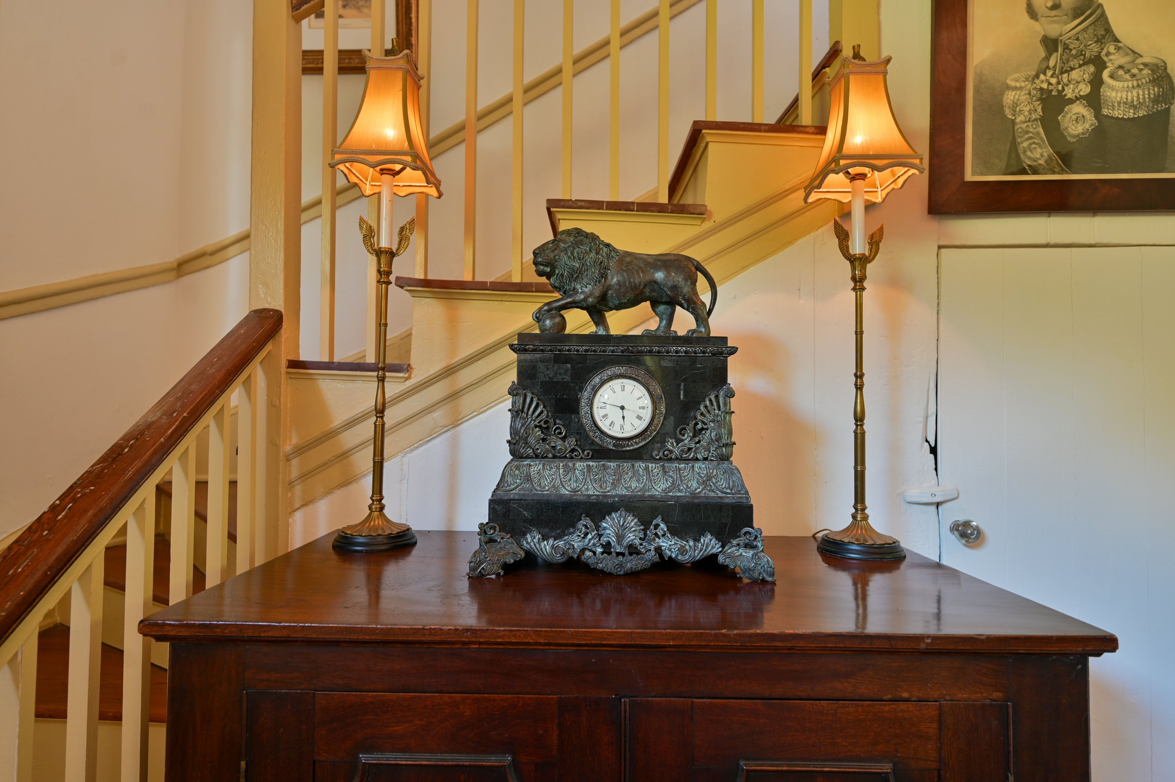 A staircase with a clock and two lamps on a wooden table.