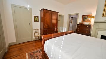 A bedroom with a large bed, wooden wardrobe, and a chair.