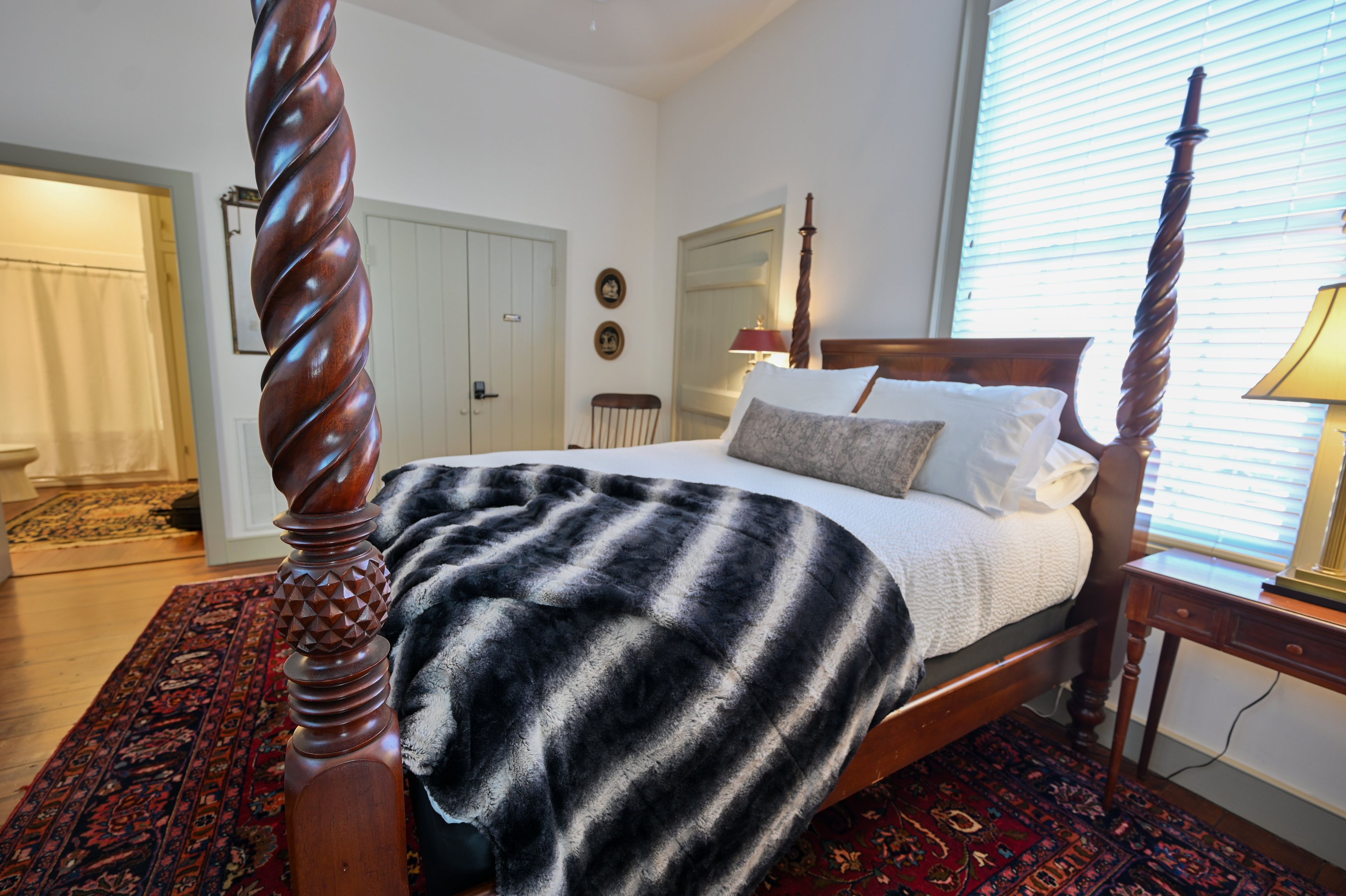Une chambre à coucher avec un lit à baldaquin, une tête de lit en bois, un tapis à motifs et une porte dotée d’un interrupteur.