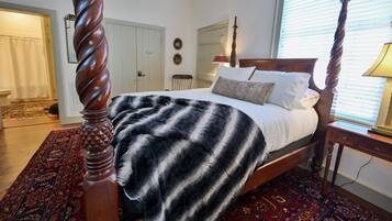 Une chambre à coucher avec un lit à baldaquin, une tête de lit en bois, un tapis à motifs et une porte dotée d’un interrupteur.