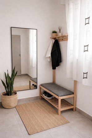 A minimalist hallway with a bench, a mirror, a potted plant, a shelf with a plant and a candle, and a woven rug. - Perfect 1-bedroom apartment with AC in awesome Tiranë (Tiranë)