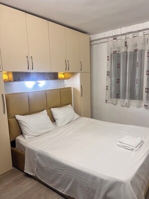 A neatly made bed with white linens, a headboard with a light fixture, and a window with curtains. - Perfect 1-bedroom apartment with AC in awesome Tiranë (Tiranë)