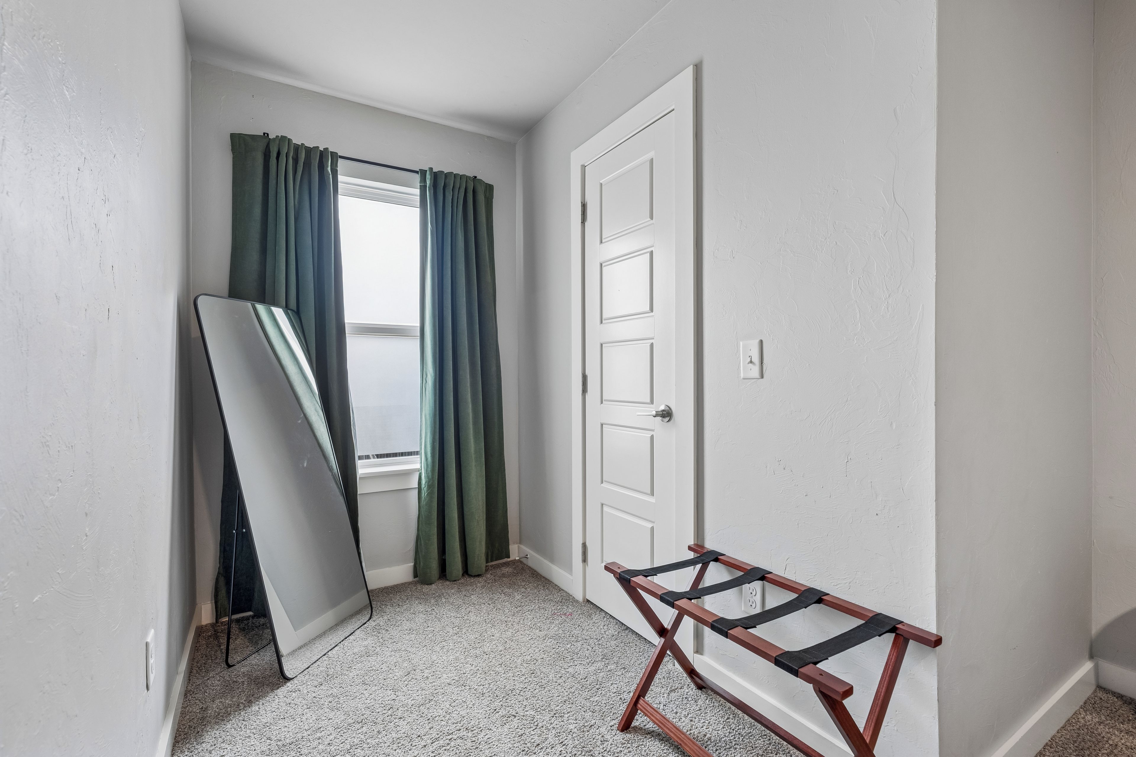 Ein Zimmer mit Tür, einem Fenster mit Vorhängen, einer Whiteboard-Tafel und einem Holzregal.
