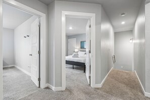 A hallway leading to a bedroom with a bed, a nightstand, and a mirror. There are white doors on either side of the hallway. - Spacious 5-bedroom house perfect for groups (Edmond)
