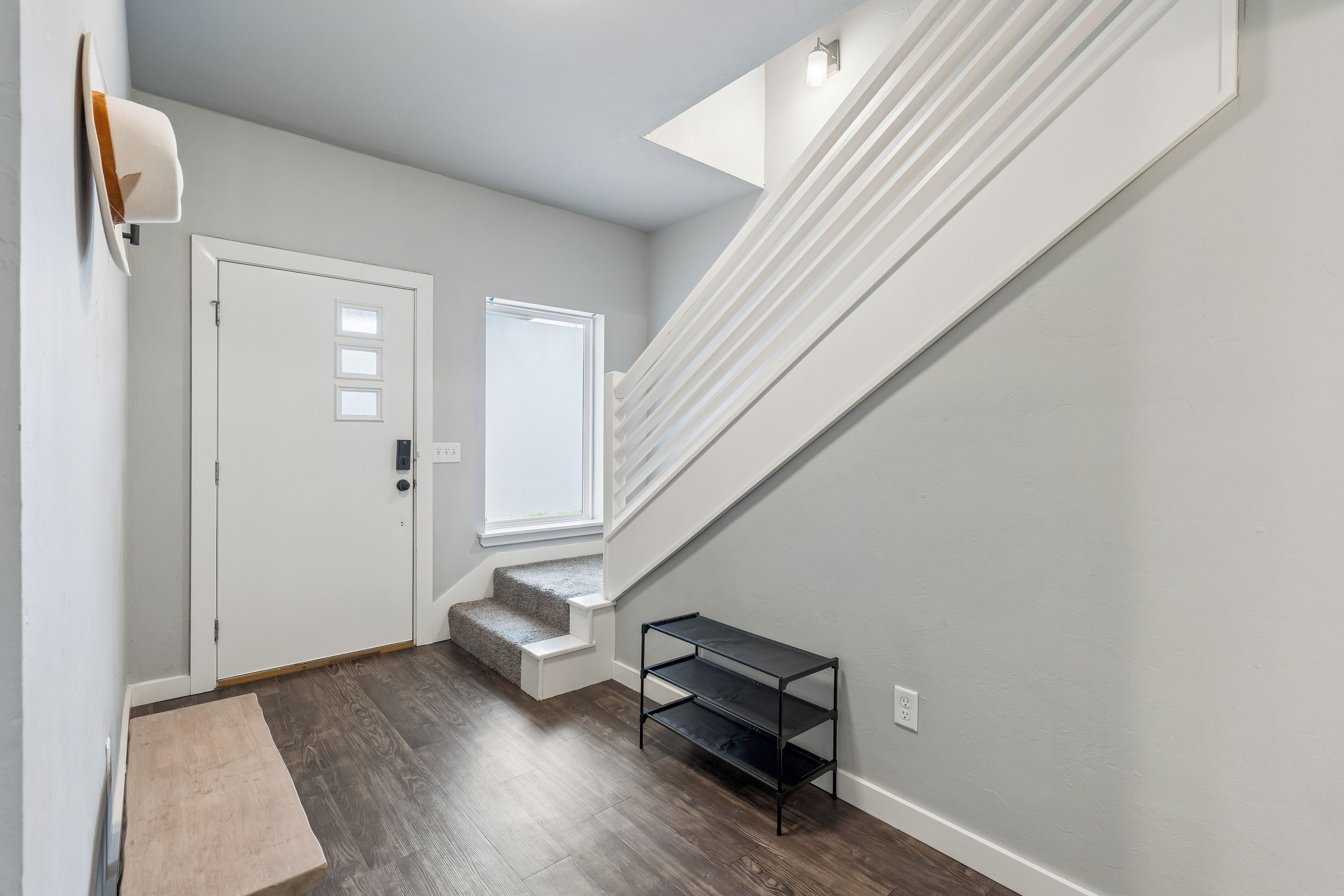 A hallway with a white door, a window, a staircase, and a small shelf.