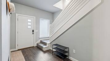 A hallway with a white door, a window, a staircase, and a small shelf.