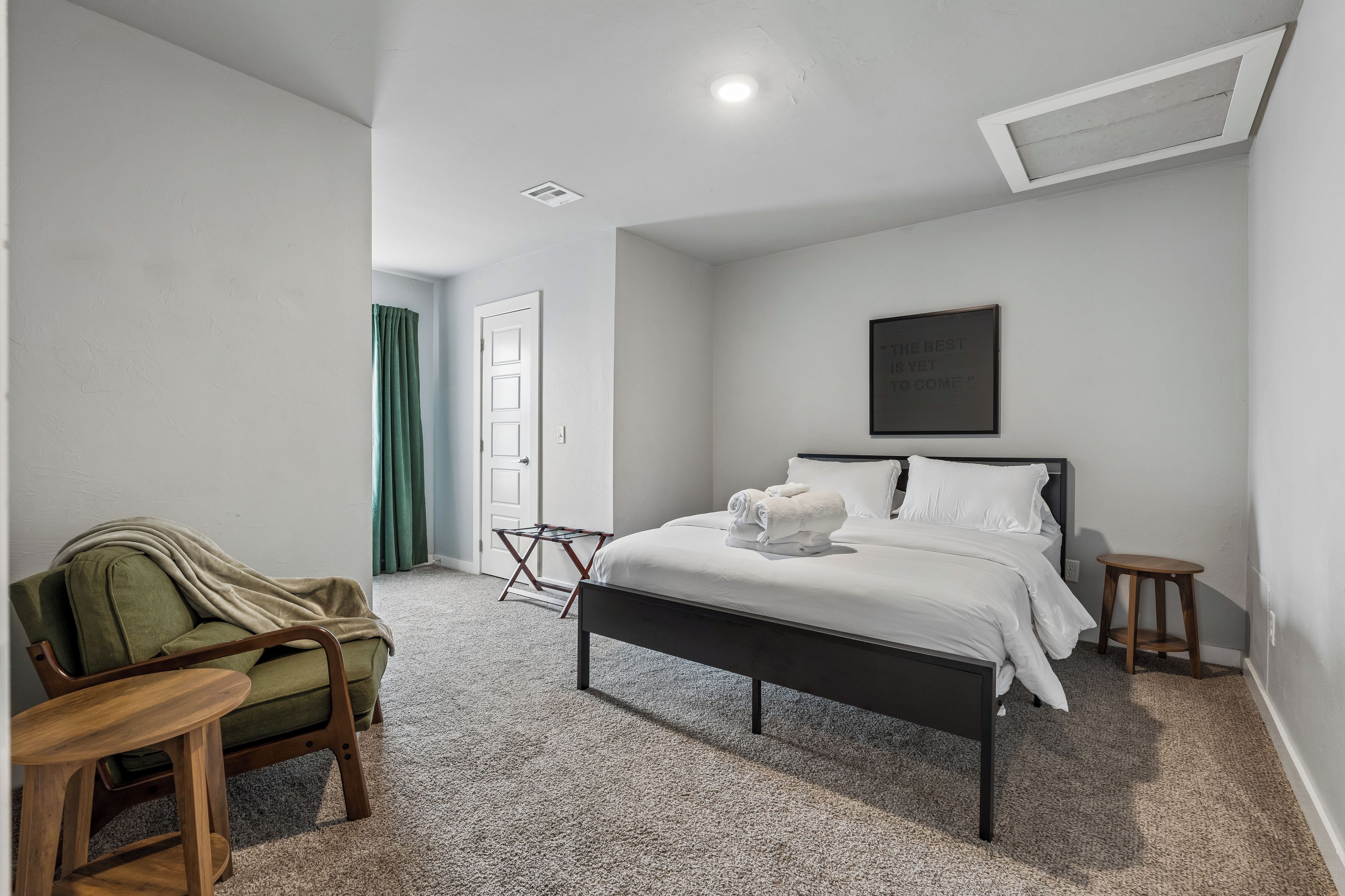 A bedroom with a bed, a chair, a small table, a door, and a wall-mounted picture.