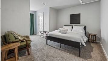A bedroom with a bed, a chair, a small table, a door, and a wall-mounted picture.