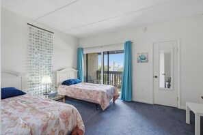 Een hotelkamer met twee bedden, een raam met gordijnen, een deur en een klein tafeltje.