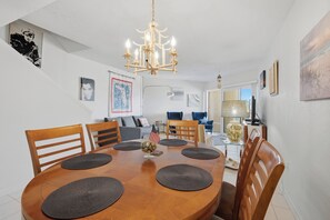 Een eethoek met een ronde houten tafel, stoelen, een kroonluchter en diverse wanddecoraties.