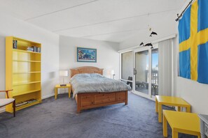 Ein Schlafzimmer mit einem Bett, einem Bücherregal, einem Schreibtisch, einer Lampe und Blick durch eine Glastür.
