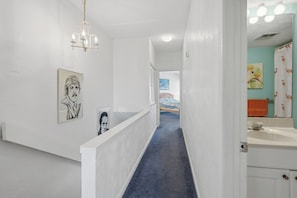 Ein Korridor mit blauem Teppich, weißen Wänden, einer Chandelüster und Kunstwerken.