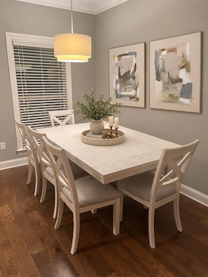 A dining area with a white table, four chairs, a hanging light fixture, and two abstract paintings on the wall. - The Grove Getaway Standalone Townhome 4BR/4.5BA Near Ole Miss (Oxford)