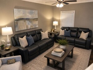 A living room with two black leather sofas, a coffee table, a floor lamp, a side table with a lamp, a vase with a plant, and a painting on the wall. - The Grove Getaway Standalone Townhome 4BR/4.5BA Near Ole Miss (Oxford)