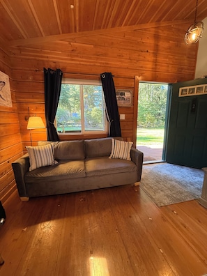 A wooden interior with a sofa, a lamp, and a door leading outside. - Captain's Cabin at Elk Meadows Cabins (Forks)