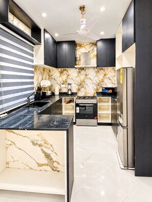 A modern kitchen with a marble backsplash, stainless steel appliances, and a black countertop. - Afro Coastal Villa  Modern 3-Bedroom En-Suite Retreat Near the Sea in Accra (Accra)