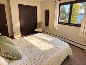 Ein Schlafzimmer mit einem großen Bett, einem Sessel, einem Kleiderschrank, einem Fenster mit Blick und einem Thermostat.