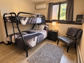 A bunk bed with a bedside table and lamp, a chair, a rug, and a window with curtains. - French Lake Shores-Sunset Retreat/Private 3 Bedroom Lakefront for 8 (Faribault)