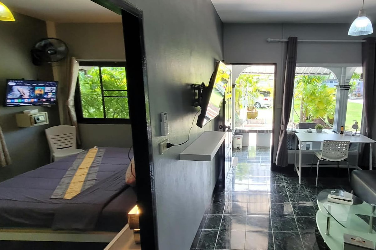 Habitació d'hotel senzilla amb llit, escriptori, taula petita, sofà amb coixins i televisió.