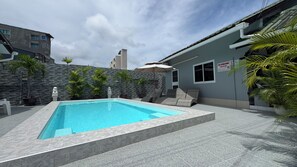 A swimming pool with a stone border, surrounded by potted plants and a stone wall. - Karon Homes (Karon)