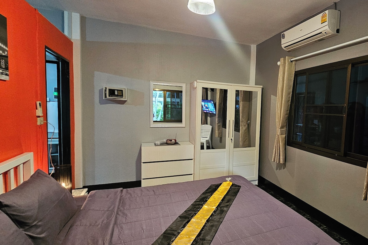 Una habitació d'hotel amb un llit, una televisió penjada a la paret, un aparell d'aire condicionat i una finestra amb cortines.